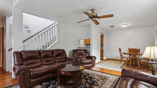 living room featuring light wood-type flooring, ceiling fan, visible vents, and stairway