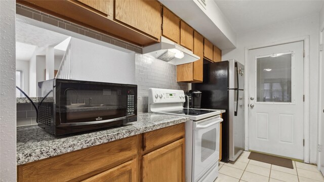 kitchen with brown cabinetry, black microwave, under cabinet range hood, white electric stove, and backsplash