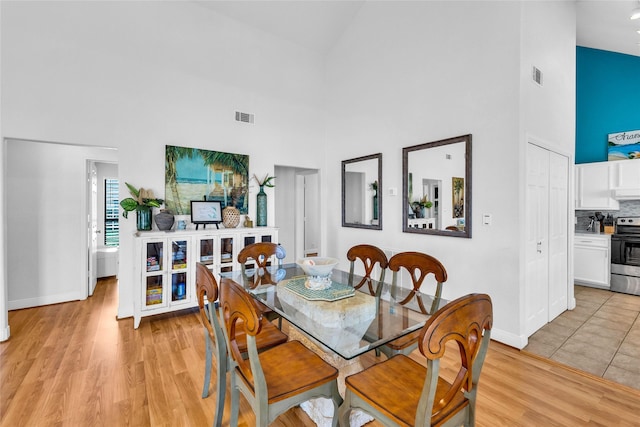 dining area featuring high vaulted ceiling, baseboards, light wood-style flooring, and visible vents