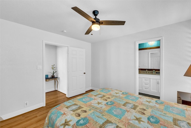 bedroom featuring a ceiling fan, wood finished floors, a sink, baseboards, and ensuite bath
