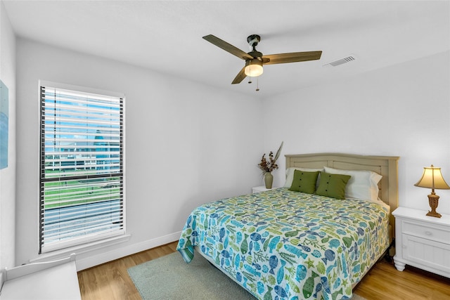 bedroom featuring visible vents, baseboards, ceiling fan, and wood finished floors
