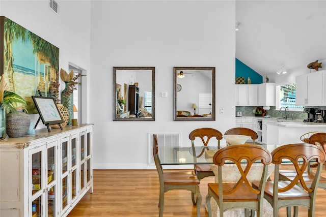 dining room with high vaulted ceiling, ceiling fan, light wood finished floors, and visible vents
