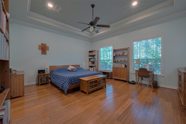 bedroom with visible vents, light wood-style flooring, crown molding, and a tray ceiling