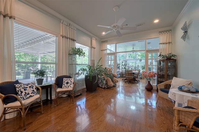 living area with crown molding, a ceiling fan, wood finished floors, and a healthy amount of sunlight