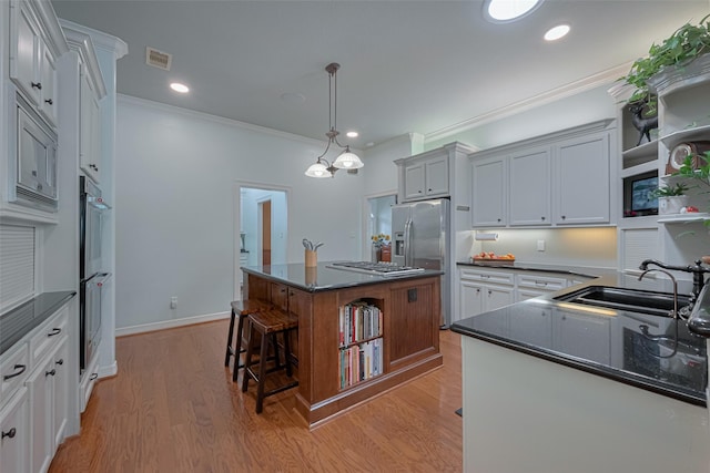 kitchen with a sink, stainless steel appliances, a kitchen island, visible vents, and ornamental molding
