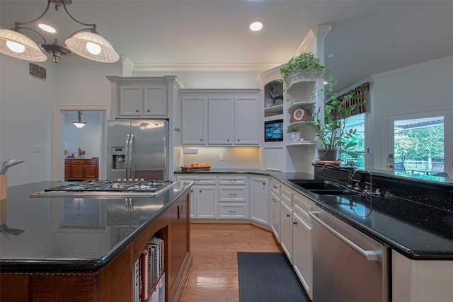 kitchen featuring crown molding, appliances with stainless steel finishes, a sink, light wood-style floors, and dark stone counters