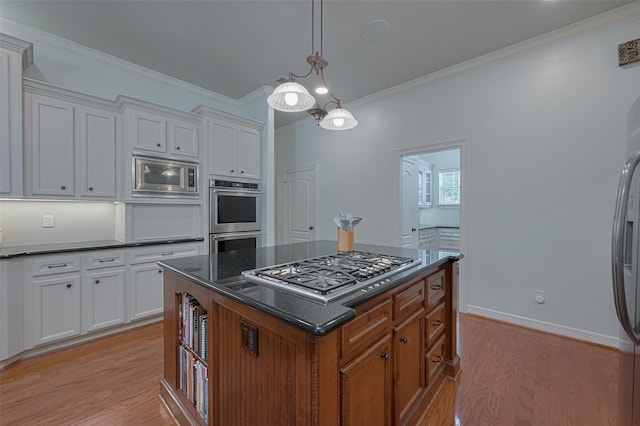 kitchen featuring appliances with stainless steel finishes, a center island, light wood finished floors, ornamental molding, and white cabinetry