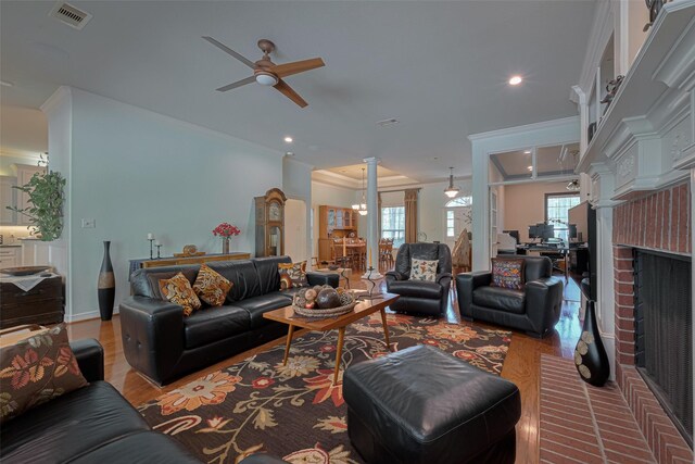 living area with visible vents, crown molding, wood finished floors, ceiling fan, and ornate columns