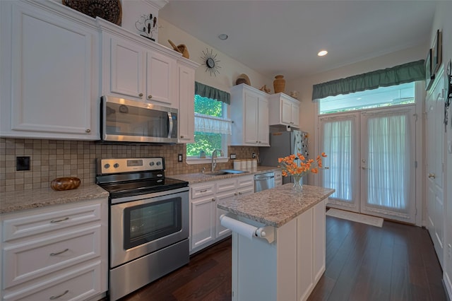 kitchen featuring dark wood-style flooring, a kitchen island, white cabinets, a sink, and stainless steel appliances