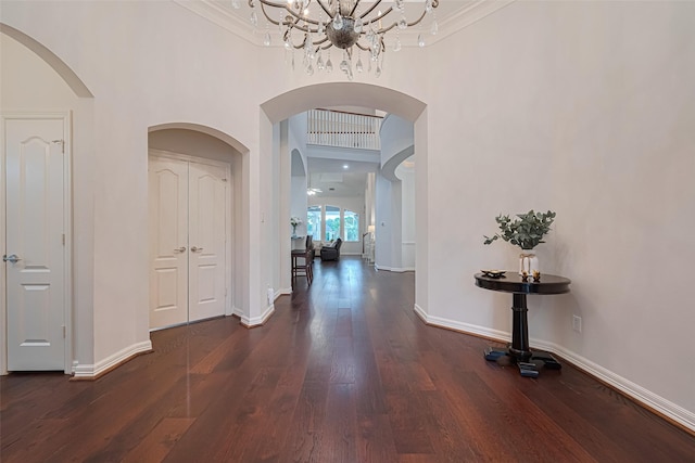 corridor featuring an inviting chandelier, arched walkways, crown molding, and a towering ceiling