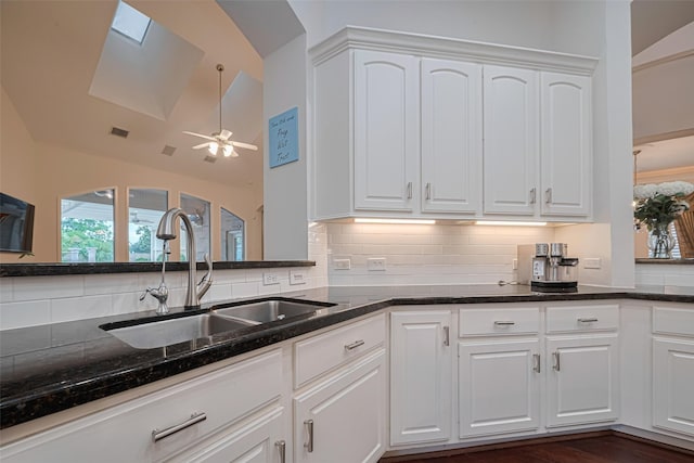 kitchen featuring white cabinetry, a sink, vaulted ceiling with skylight, and tasteful backsplash