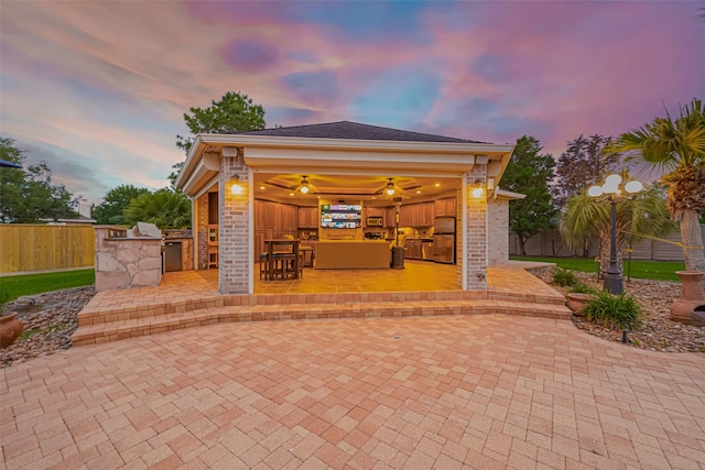 outdoor structure at dusk featuring a fenced backyard, outdoor dry bar, and exterior kitchen