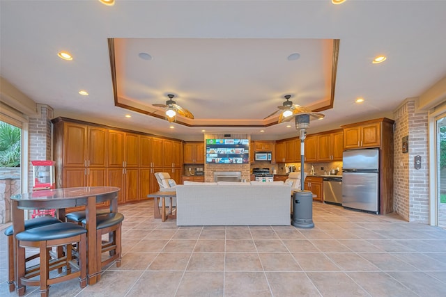 kitchen featuring ceiling fan, appliances with stainless steel finishes, brown cabinetry, and a raised ceiling