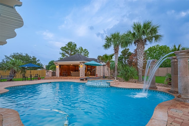 view of swimming pool featuring a pool with connected hot tub, fence, a patio area, and outdoor dry bar