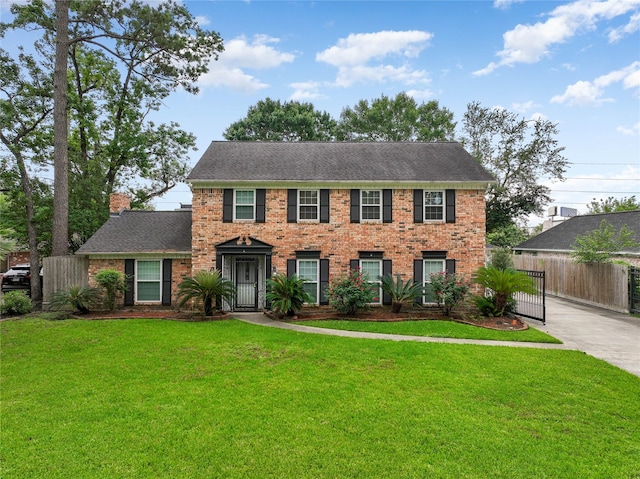 colonial house with brick siding, fence, a chimney, and a front lawn