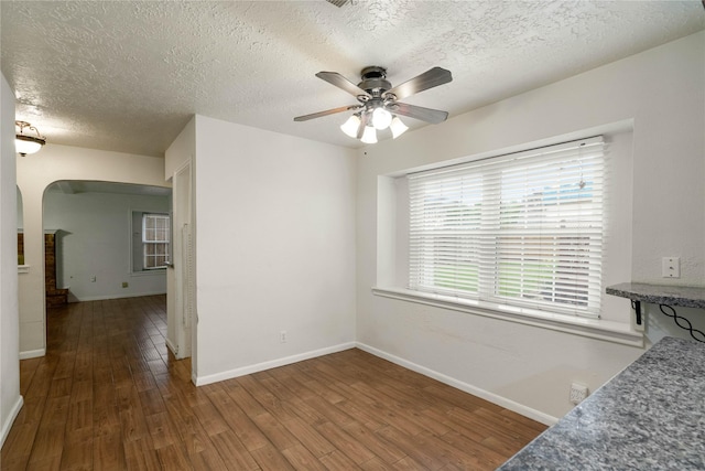 unfurnished dining area featuring ceiling fan, a textured ceiling, arched walkways, wood finished floors, and baseboards