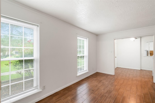 spare room with baseboards, ornamental molding, a textured ceiling, and wood finished floors