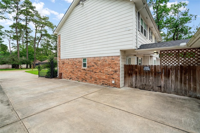 view of home's exterior with brick siding, a gate, a patio area, and fence