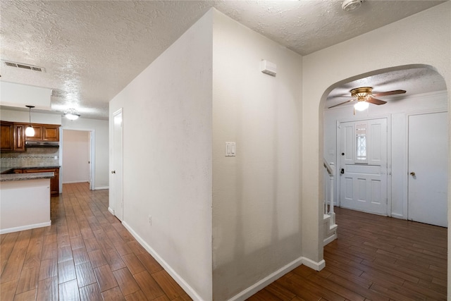 hallway featuring dark wood-style flooring, arched walkways, a textured ceiling, baseboards, and visible vents