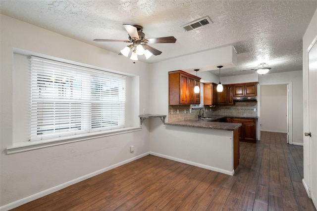 kitchen with brown cabinets, a sink, a peninsula, a ceiling fan, and visible vents