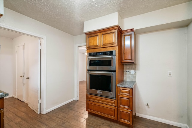 kitchen featuring brown cabinets, stainless steel double oven, baseboards, decorative backsplash, and dark wood-style floors