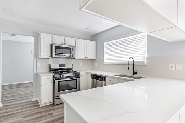 4523 Natural Bridge Dr, Kingwood, TX 77345 - kitchen with stainless steel appliances, a sink, light stone countertops, white cabinets, and light wood-type flooring