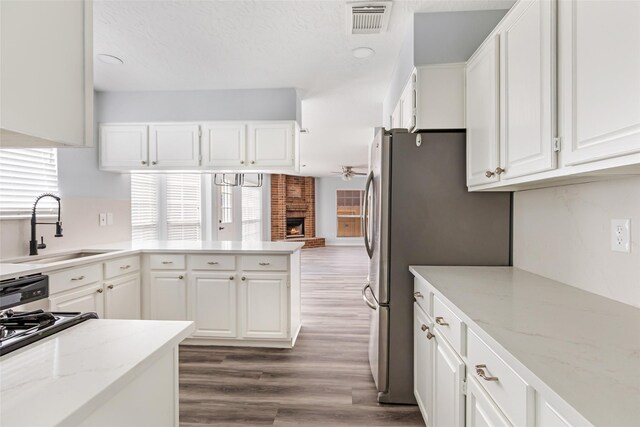 4523 Natural Bridge Dr, Kingwood, TX 77345 - kitchen featuring a sink, white cabinets, freestanding refrigerator, dark wood-type flooring, and a fireplace