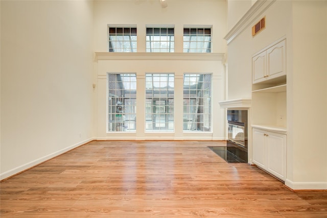 16 Treverstone Ct, Sugar Land, TX 77479 - unfurnished living room with visible vents, light wood-type flooring, baseboards, a high ceiling, and a premium fireplace