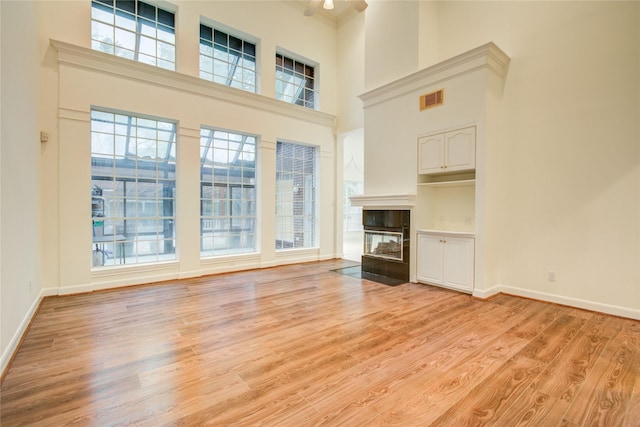 16 Treverstone Ct, Sugar Land, TX 77479 - unfurnished living room featuring visible vents, a towering ceiling, a healthy amount of sunlight, a multi sided fireplace, and light wood-style flooring