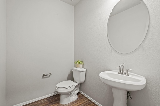 half bathroom with toilet, baseboards, a sink, and wood finished floors