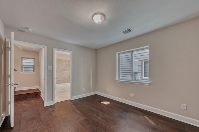 unfurnished bedroom featuring baseboards, ensuite bathroom, dark wood finished floors, and visible vents