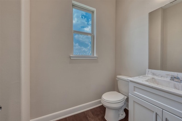 half bath with toilet, baseboards, wood finished floors, and vanity