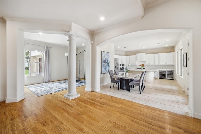 dining space featuring decorative columns, crown molding, arched walkways, light wood-type flooring, and recessed lighting