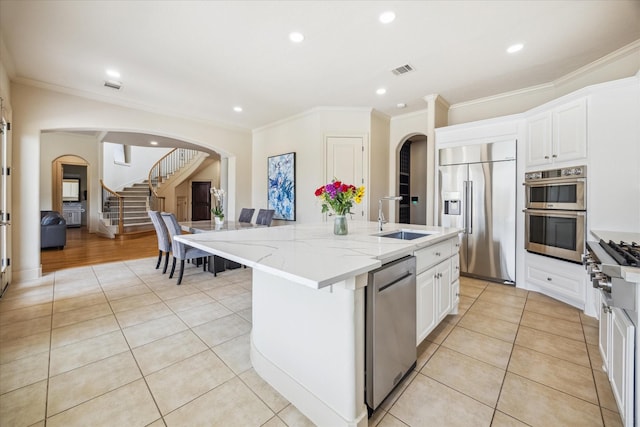 kitchen with visible vents, a sink, light stone countertops, arched walkways, and stainless steel appliances