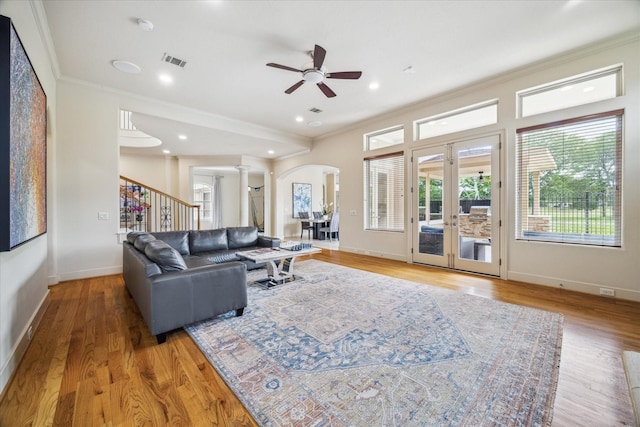 living room with decorative columns, a ceiling fan, visible vents, crown molding, and arched walkways