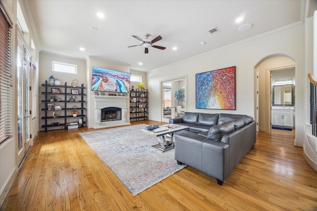 living area featuring visible vents, crown molding, a fireplace, light wood-style floors, and ceiling fan