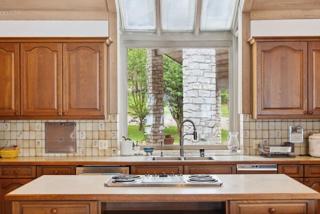 kitchen with brown cabinetry, a sink, electric stovetop, and light countertops