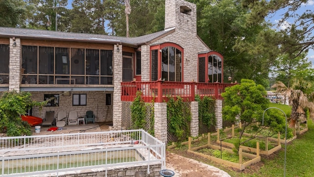 rear view of property with stone siding, a sunroom, a vegetable garden, a chimney, and a patio area