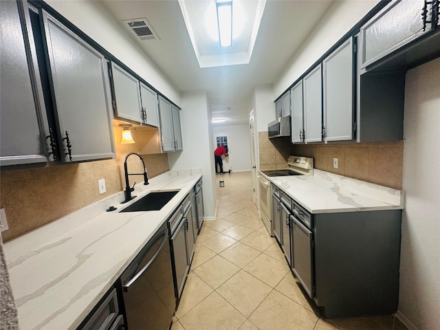kitchen with light stone countertops, a sink, stainless steel appliances, decorative backsplash, and visible vents