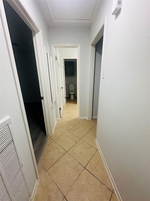 hallway with baseboards, light tile patterned floors, and attic access