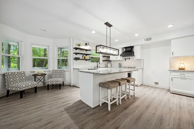 kitchen featuring visible vents, decorative backsplash, wood finished floors, wall chimney exhaust hood, and white cabinetry
