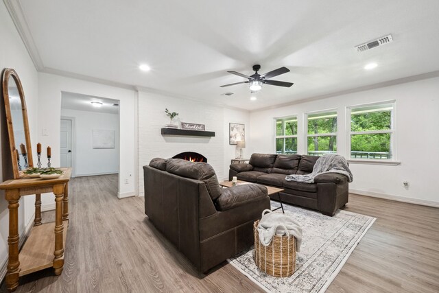 living room with a ceiling fan, visible vents, ornamental molding, and light wood finished floors