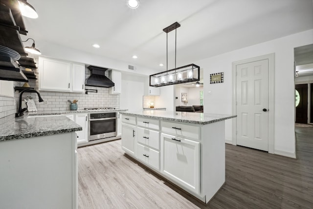 kitchen featuring wall chimney range hood, appliances with stainless steel finishes, a sink, tasteful backsplash, and a kitchen island