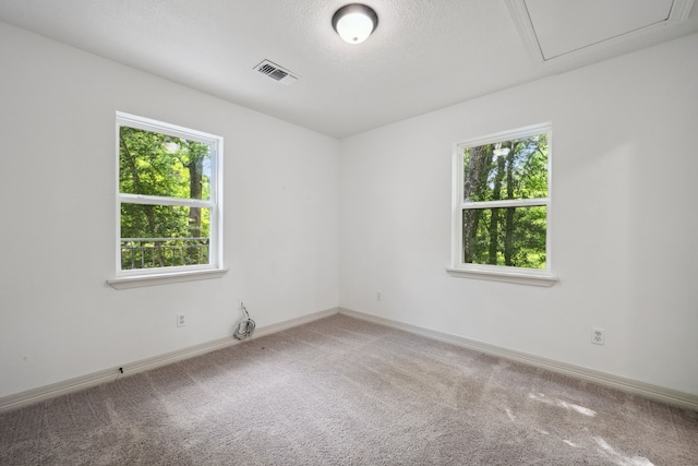 carpeted empty room with a healthy amount of sunlight, baseboards, attic access, and visible vents