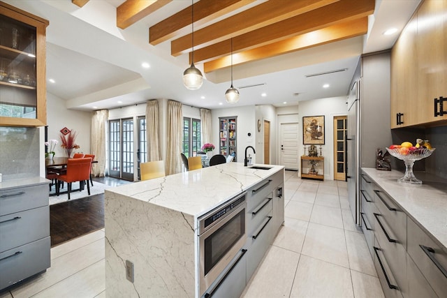 kitchen featuring a kitchen island with sink, light tile patterned flooring, stainless steel microwave, and light stone counters