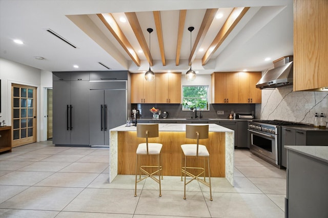 kitchen with high quality appliances, a sink, wall chimney exhaust hood, tasteful backsplash, and visible vents