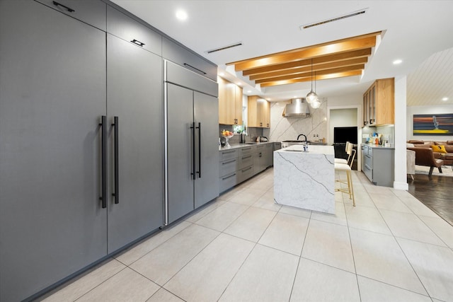 kitchen featuring a sink, wall chimney exhaust hood, a center island with sink, and gray cabinetry