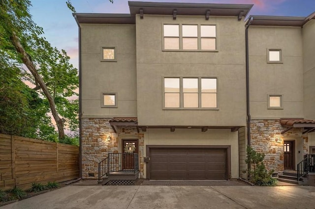 view of front of property featuring fence, stucco siding, an attached garage, and stone siding