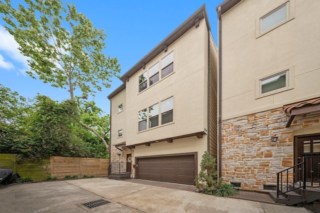 rear view of house featuring an attached garage, fence, stucco siding, and stone siding