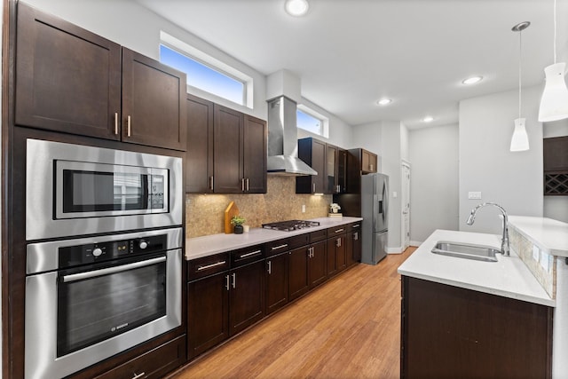 kitchen with wall chimney range hood, a sink, light wood finished floors, light countertops, and stainless steel appliances